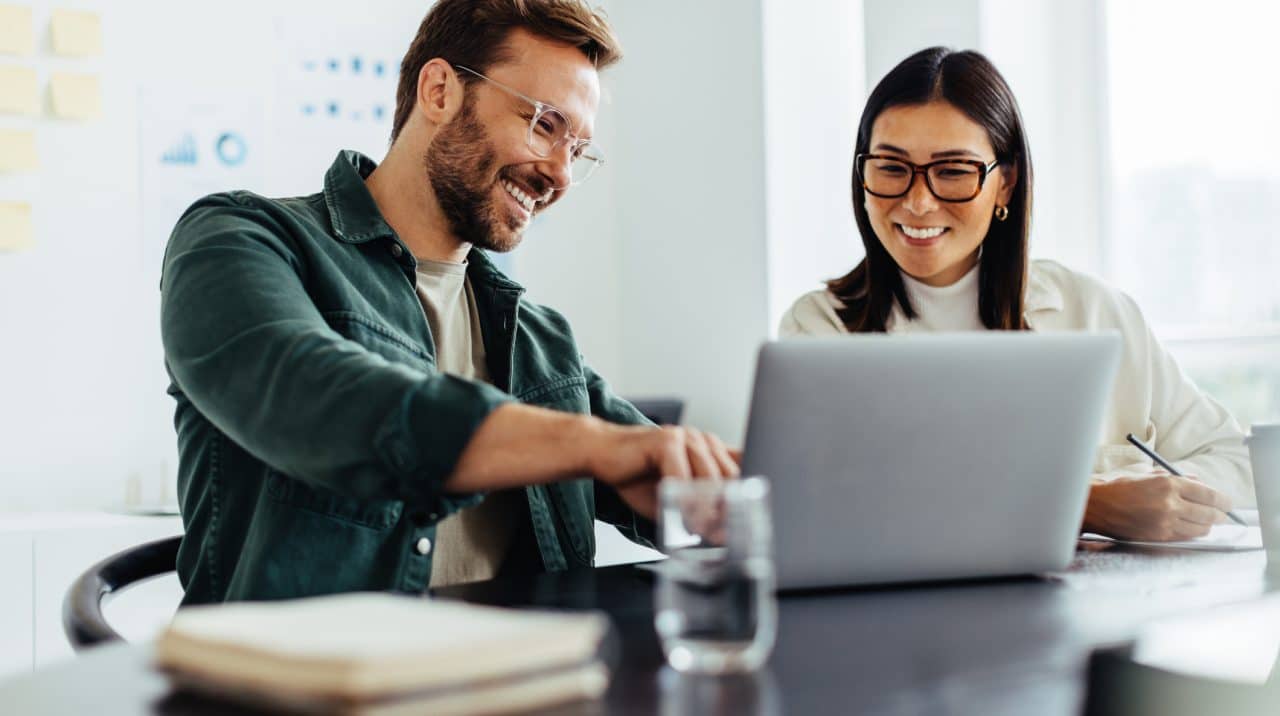 Two business people using a laptop together while sitting in a meeting. Happy business people looking at a slide presentation in an office.