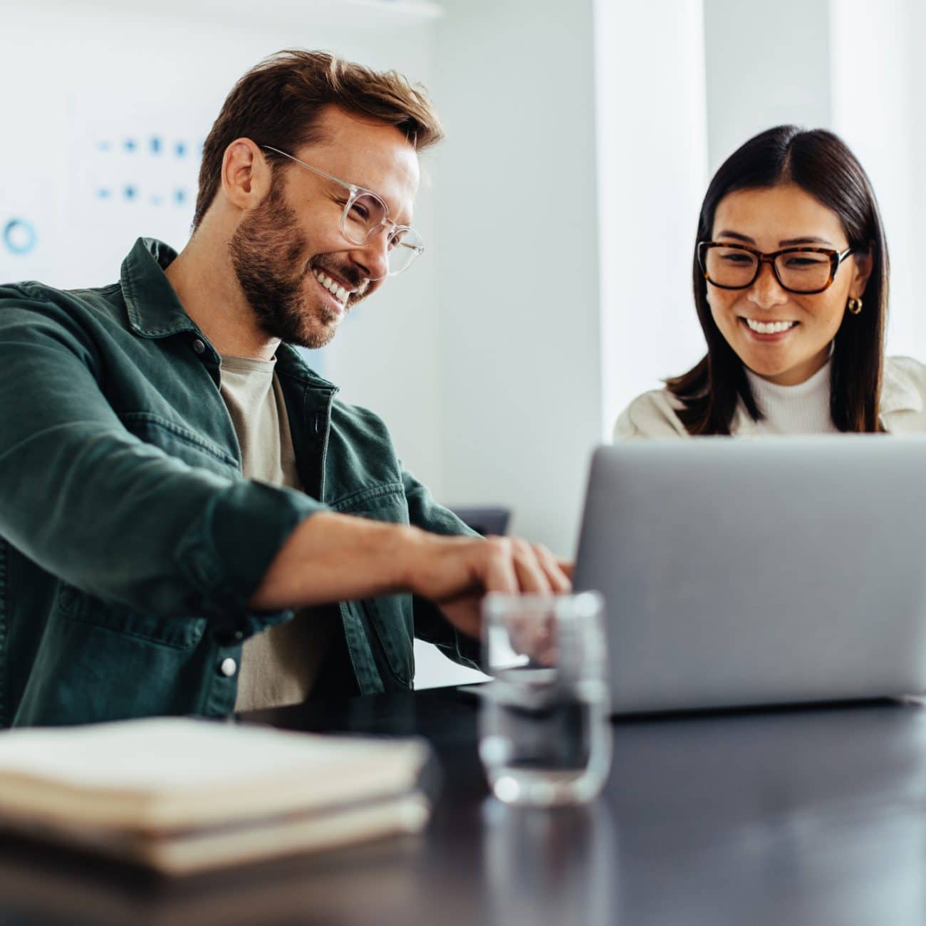 Two business people using a laptop together while sitting in a meeting. Happy business people looking at a slide presentation in an office.