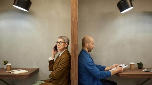 Twee zakenmensen die aan bureau's zitten gescheiden door een tussenmuur